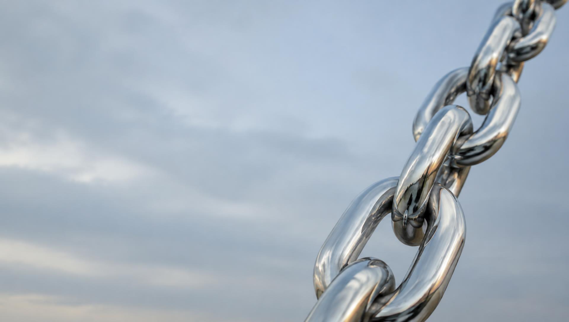 Polished chrome chain links against a soft blue-grey sky